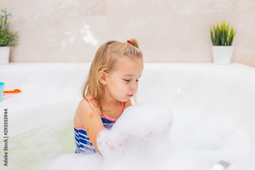 Little blonde smiling girl taking bubble bath in beautiful bathroom.Kids hygiene. Shampoo, hair treatment and soap for children. Kid bathing Little blonde smiling girl taking bubble bath in beautiful bathroom.Kids hygiene. Shampoo, hair treatment and soap for children. Kid bathing