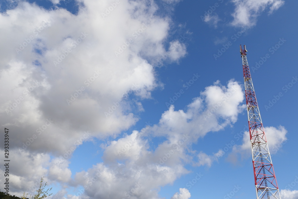 Obraz premium Telecommunications tower on light blue sky background and white club clouds