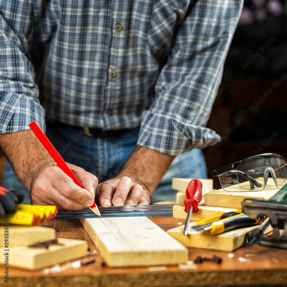 Adult craftsman carpenter with pencil and ruler tracing the cutting line on a wooden table. Housework do it yourself. Stock photography.