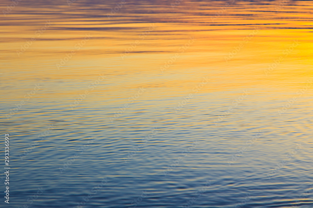 Clear water texture in blue and orange. Background of the ocean and the sea backlit by the sun. Soft waves. Natural water