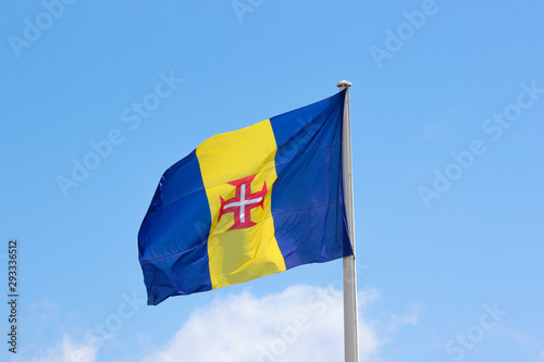 Waving flag of Madeira with blue sky in the background. It consists of a blue-gold-blue vertical triband with a red-bordered white Cross of Christ in the center. Portuguese island in Atlantic ocean photo