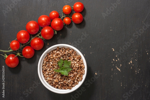 Buckwheat porridge with cherry tomatoes on black wood background with сopy space 