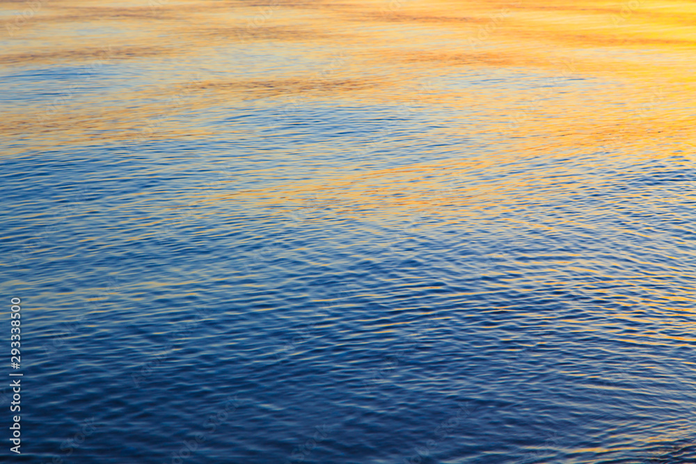 Clear water texture in blue and orange. Background of the ocean and the sea backlit by the sun. Soft waves. Natural water Clear water texture in blue and orange. Background of the ocean and the sea backlit by the sun. Soft waves. Natural water