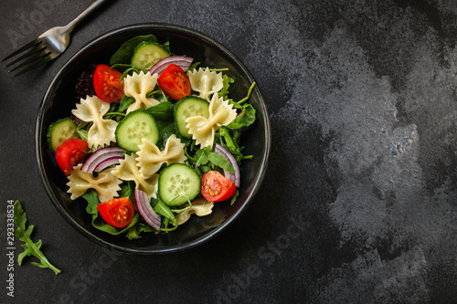 italian pasta salad farfalle, vegetables, mix leaves (tomato, cucumber, onion, lettuce, chard, arugula and more) menu concept. food background. copy space. Top view