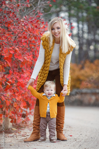 Mother and baby play in autumn park. Parent and child walk in the forest on a sunny fall day. Children playing outdoors with yellow maple leaf. Toddler boy play with golden leaves. Mom hugging kid.Hap