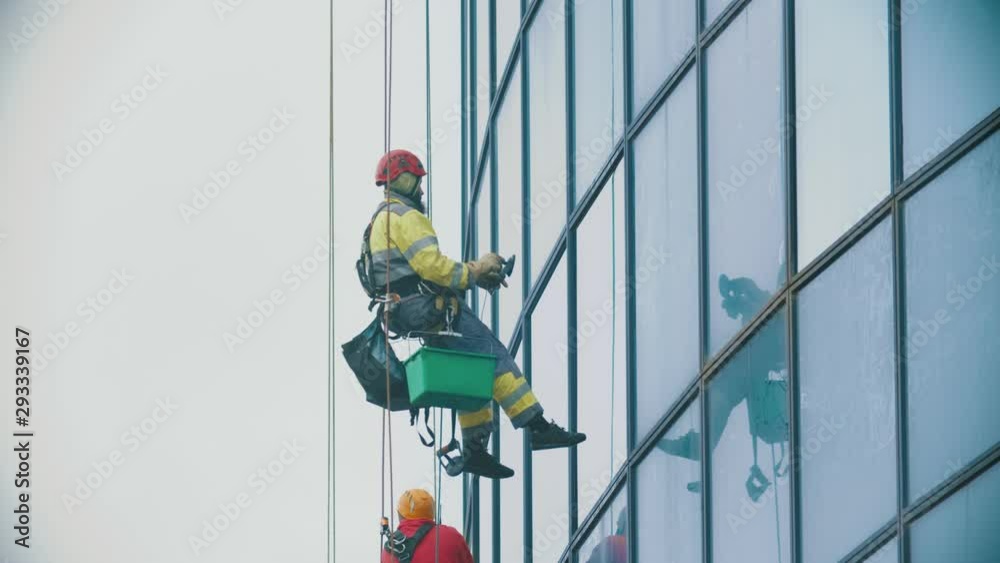 Workers hanging on ropes and wipes the exterior windows of a business skyscraper - attaching a device on the glass - industrial alpinism - overcast weather