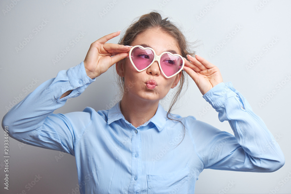 Cool Asian girl in heart-shaped glasses fools around and poses on a white background, pulls her lips into a straw, pretends to kiss Cool Asian girl in heart-shaped glasses fools around and poses on a white background, pulls her lips into a straw, pretends to kiss