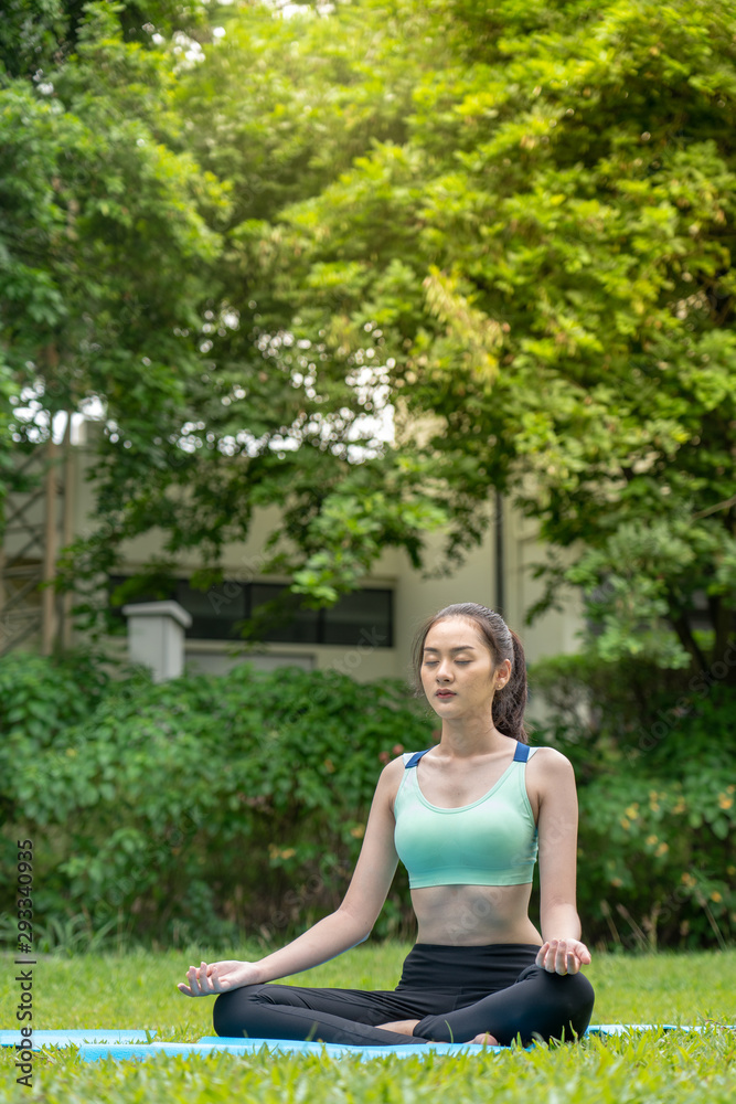 Young woman in the sportswear is practicing yoga, meditating on the blue PVC mat. In the lawn to maintain body balance, in the morning, healthy lifestyle concept. Young woman in the sportswear is practicing yoga, meditating on the blue PVC mat. In the lawn to maintain body balance, in the morning, healthy lifestyle concept.