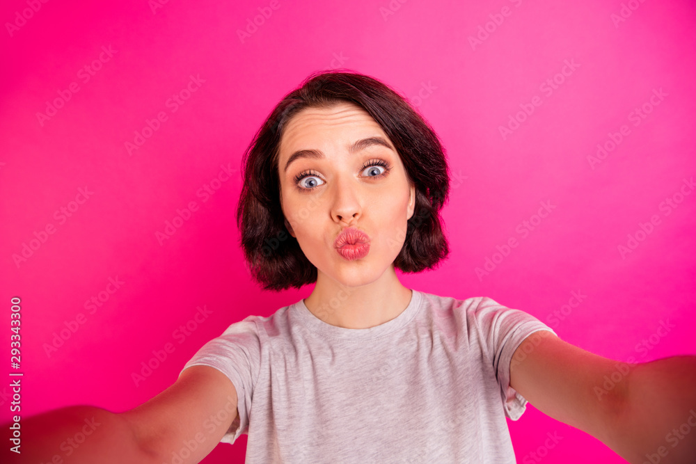 Self portrait of pretty cute charming fascinating girlfriend kissing you through air while recording video taking selfie wearing grey t-shirt isolated over fuchsia vivid color background