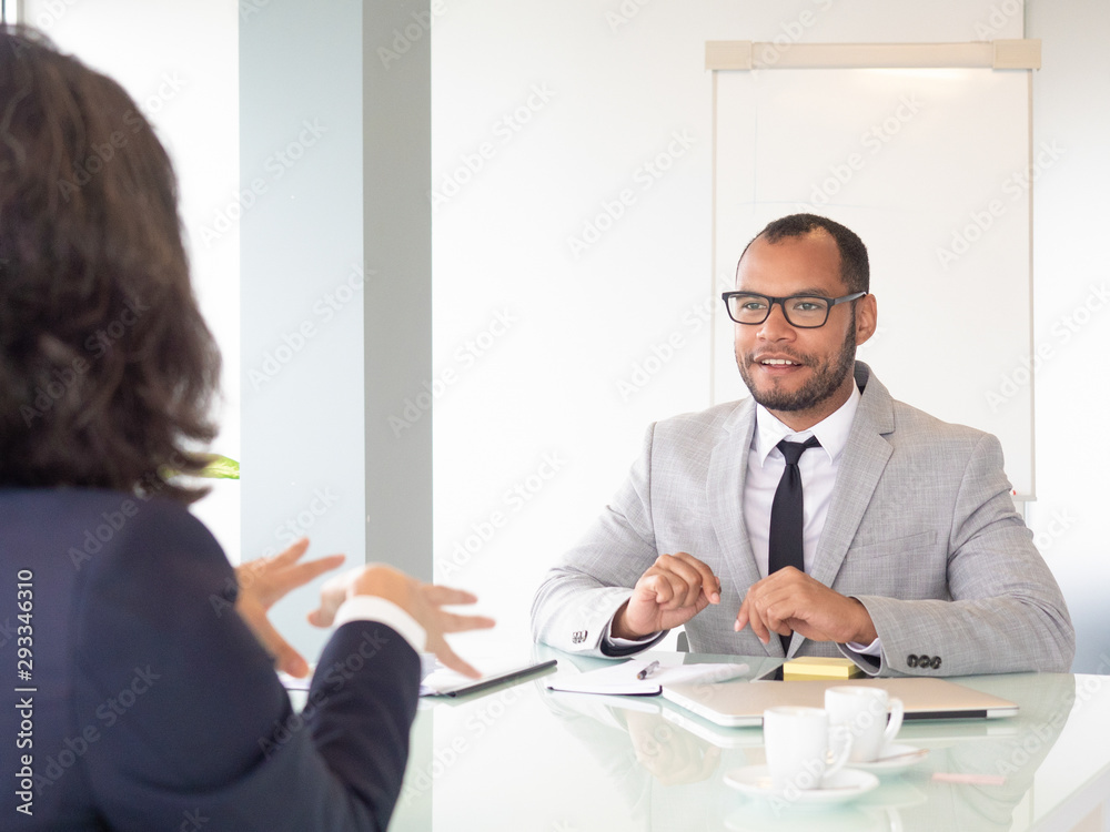 Smiling businessman talking with colleague. Young African American businessman in eyeglasses sitting at table with female colleague during business meeting. Job interview concept