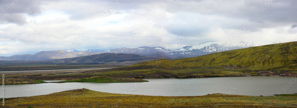 Panorama. Icelandic landscape. River, mountains, heavy clouds. Summer. Afternoon. Flat green ground