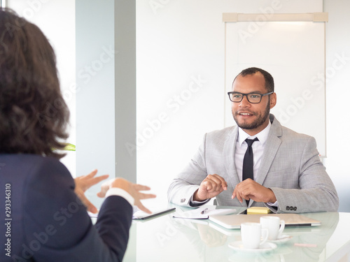 Smiling businessman talking with colleague. Young African American businessman in eyeglasses sitting at table with female colleague during business meeting. Job interview concept
