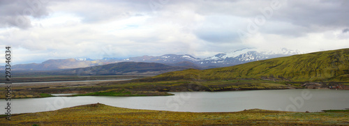 Panorama. Icelandic landscape. River, mountains, heavy clouds. Summer. Afternoon. Flat green ground