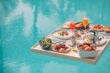 Breakfast in swimming pool, floating breakfast in tropical resort. Table relaxing in calm pool water, healthy breakfast and fruit plate by resort pool. Exotic summer diet. Tropical beach lifestyle