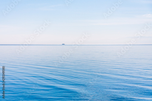 Light and simple landscape with blue sky, light clouds and wavy blue water with a ship in a distance