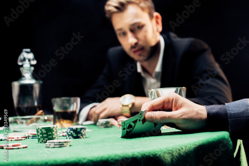 cropped view of man touching playing cards near player isolated on black