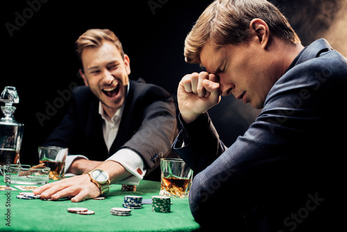 selective focus of upset man with closed eyes near winner on black with smoke