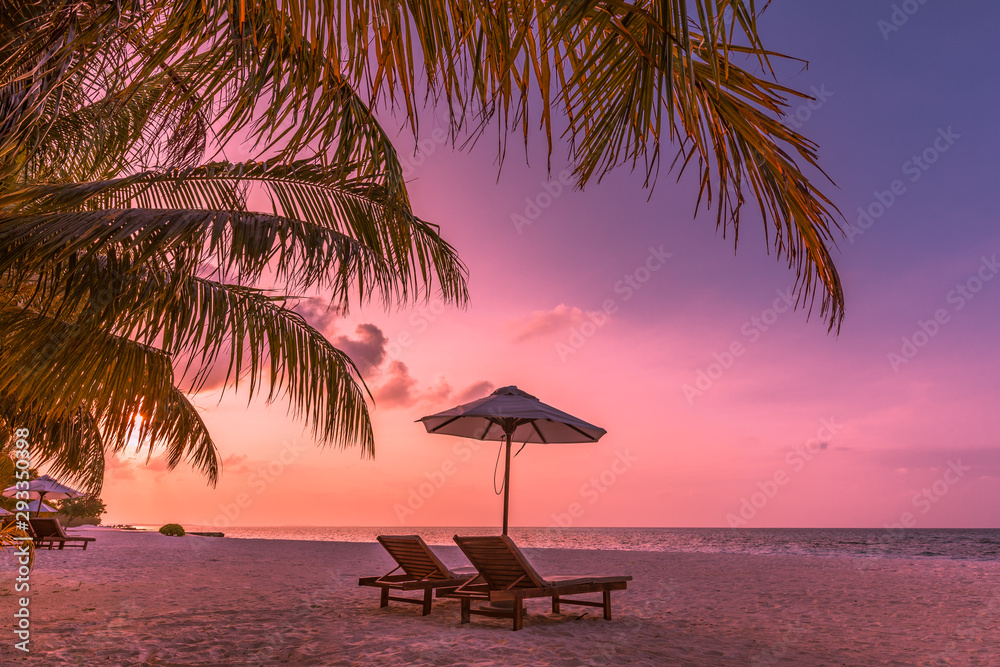 Obraz premium Twilight sky, sunrise or sunset beach view. Two loungers and umbrella under palm leaves. Luxury summer vacation background. Inspirational beach view, wonderful scenery