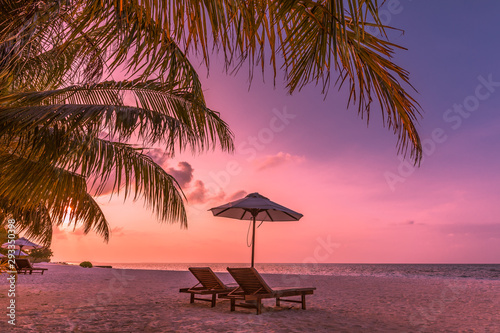 Twilight sky, sunrise or sunset beach view. Two loungers and umbrella under palm leaves. Luxury summer vacation background. Inspirational beach view, wonderful scenery