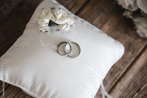  silver wedding rings on a white silk pillow with roses on a wooden surface with roses in the background