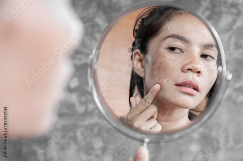 Asian woman having skin problem checking her face with dark spot, freckle from uv light in mirror photo