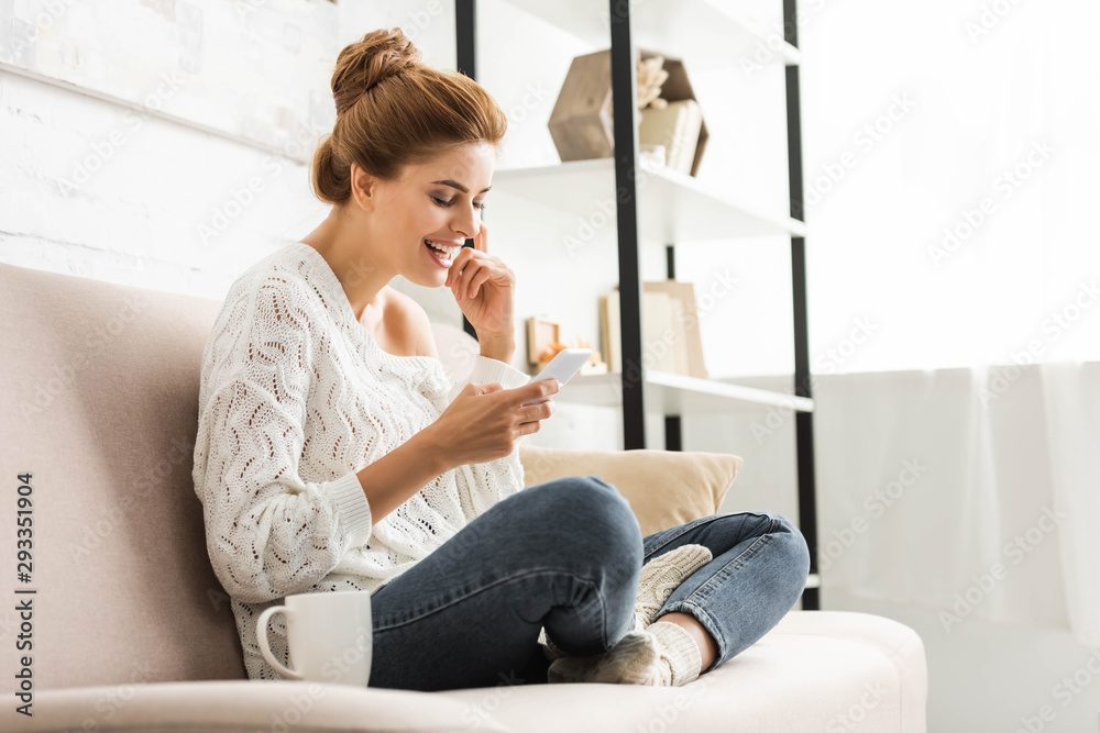 attractive woman in white sweater smiling and using smartphone attractive woman in white sweater smiling and using smartphone