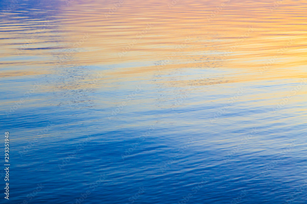 Clear water texture in blue and orange. Background of the ocean and the sea backlit by the sun. Soft waves. Natural water Clear water texture in blue and orange. Background of the ocean and the sea backlit by the sun. Soft waves. Natural water