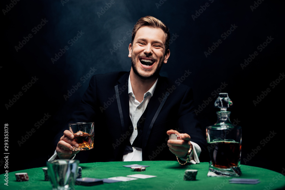selective focus of cheerful man holding glass with alcohol on black with smoke selective focus of cheerful man holding glass with alcohol on black with smoke