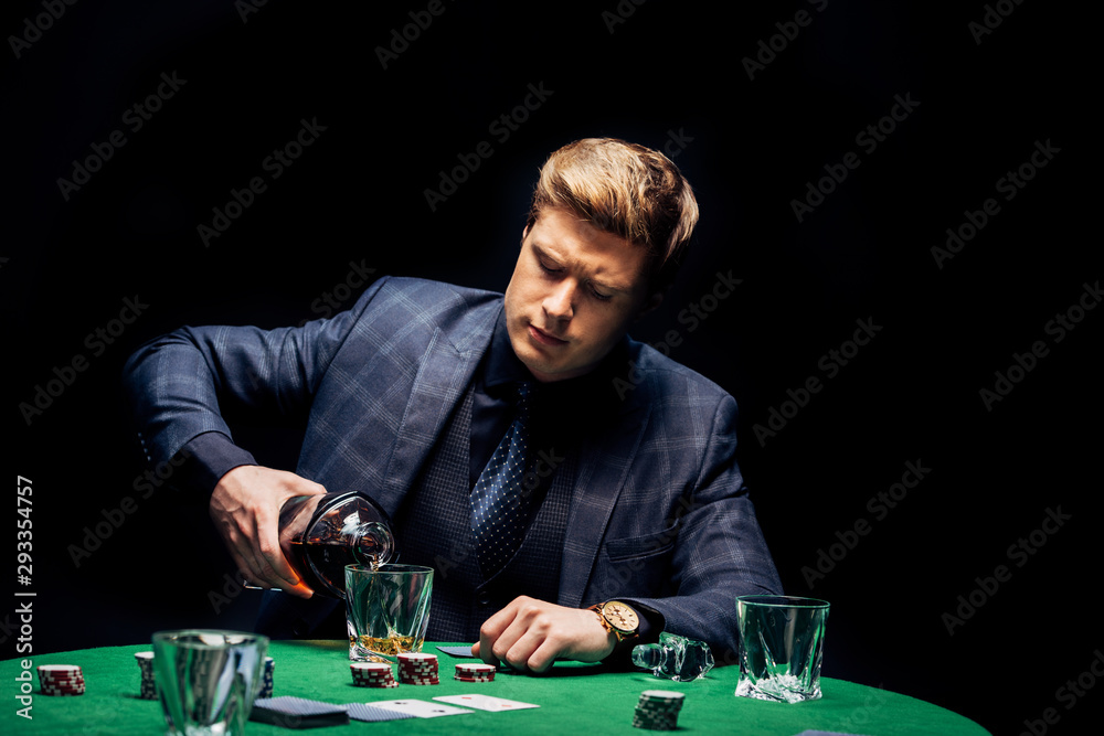 selective focus of handsome man pouring whiskey in glass near playing cards isolated on black selective focus of handsome man pouring whiskey in glass near playing cards isolated on black
