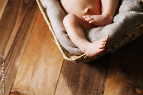 legs of a baby lying in a basket on a wooden floor