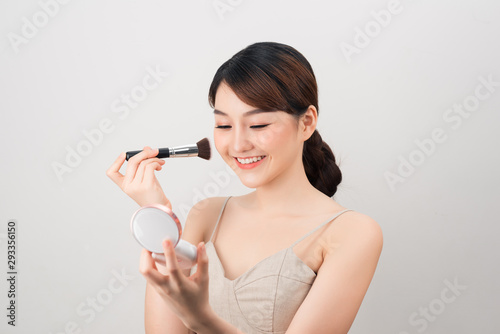 Portrait of a young beautiful woman applying foundation with black brush.
