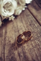 Beautiful toned picture with wedding rings lie on a wooden surface against the background of a bouquet of flowers