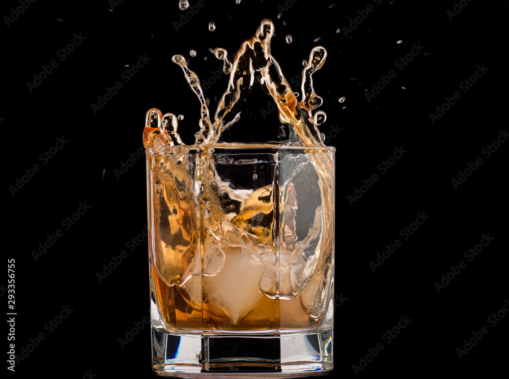 Drops of ice in a glass with whiskey on a black background, splashes and drops Drops of ice in a glass with whiskey on a black background, splashes and drops