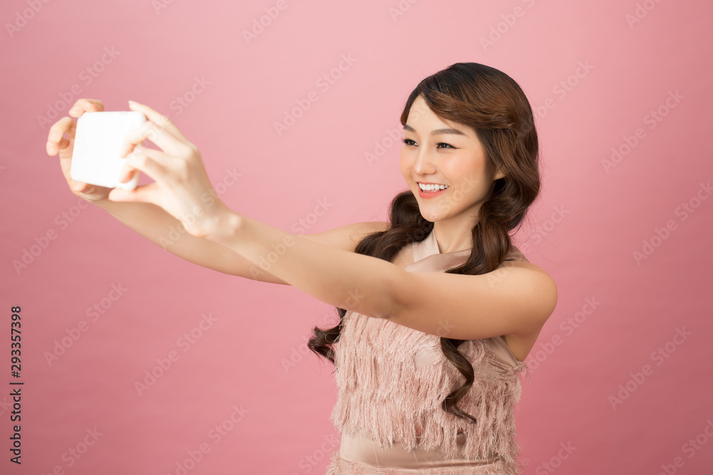 Studio portrait of beautiful woman smiling with white teeth and making selfie, photographing herself over pink background Studio portrait of beautiful woman smiling with white teeth and making selfie, photographing herself over pink background