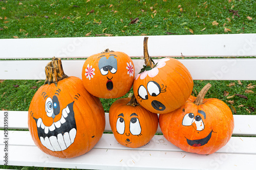 Many pumpinks with painted faces on white porch.