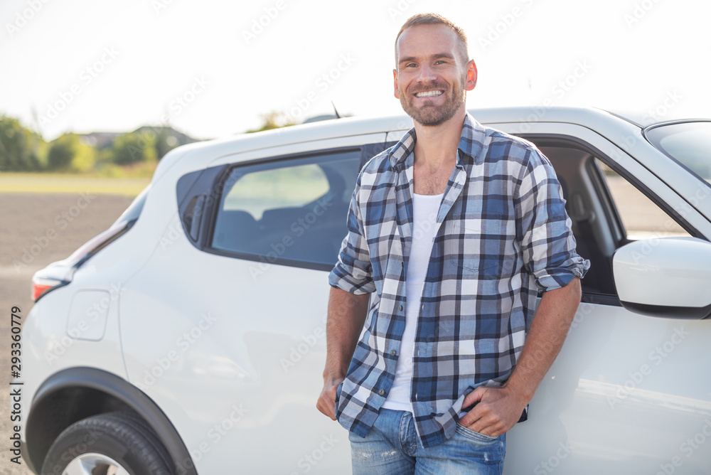 An attractive young man stands near a white car. An attractive young man stands near a white car.