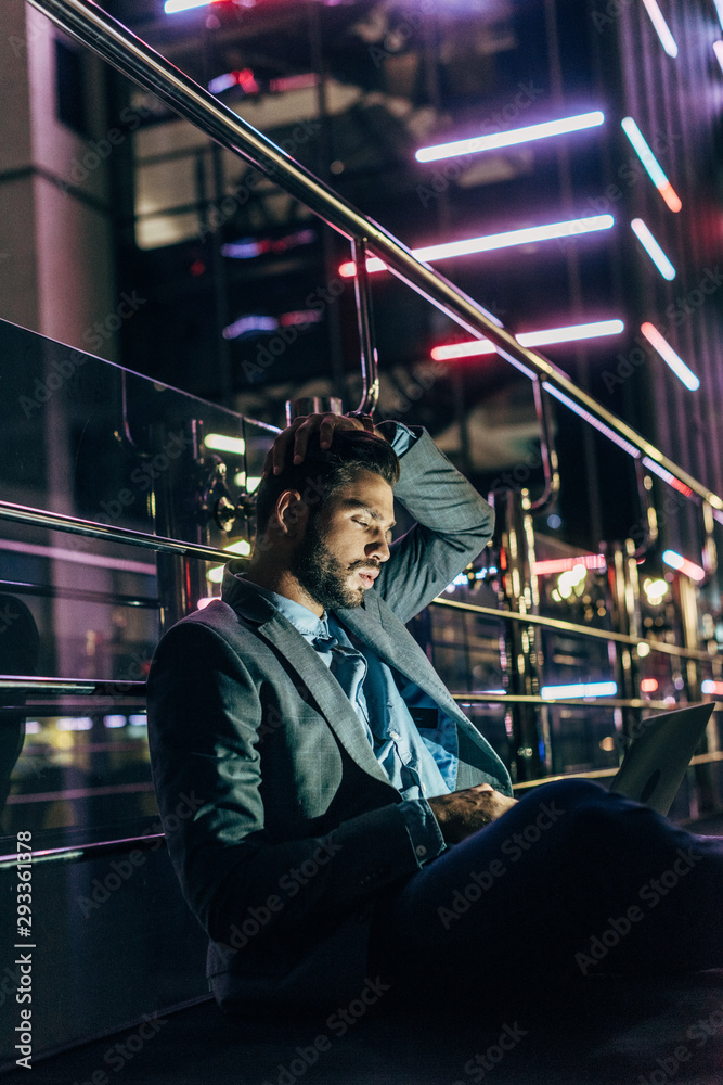 handsome businessman in formal wear sitting and using laptop in night city
