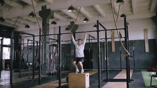 The athletic body is in good shape, best exercises in gym. Blonde sportsman pulls up on gym horizontal bar. use box. Effective exercises in gym without injuries, calisthenics and morning exercises.