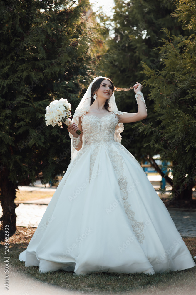 Likable and pretty bride in a white wedding dress with a wedding bouquet in his hands on a enjoying romantic moments outside on a summer. Wedding day.  Dreamy bride hold  beautiful bouquet