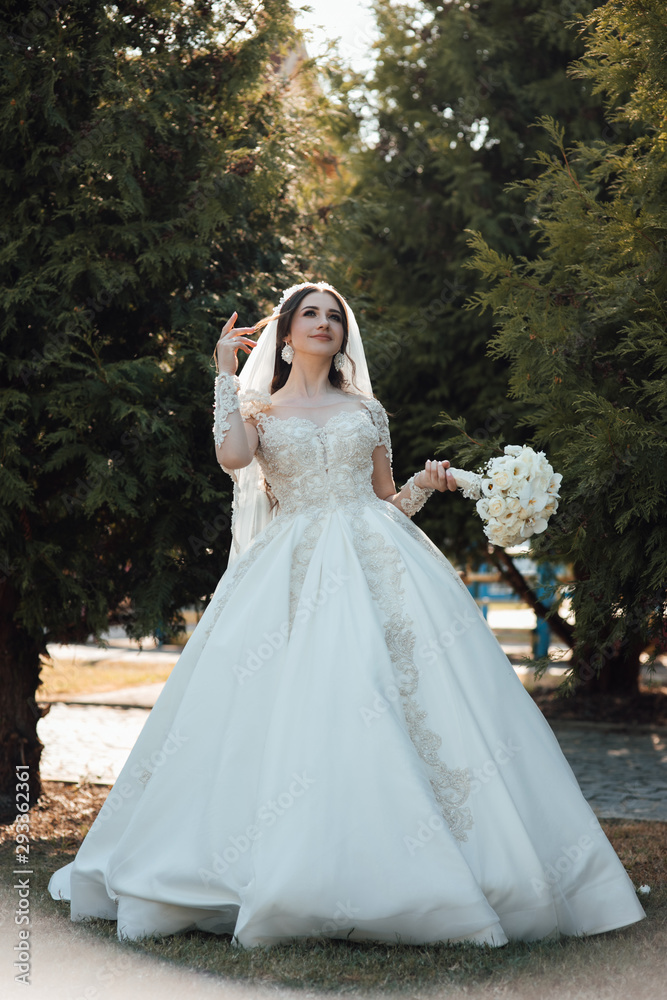 Likable and pretty bride in a white wedding dress with a wedding bouquet in his hands on a enjoying romantic moments outside on a summer. Wedding day. Dreamy bride hold beautiful bouquet Likable and pretty bride in a white wedding dress with a wedding bouquet in his hands on a enjoying romantic moments outside on a summer. Wedding day. Dreamy bride hold beautiful bouquet