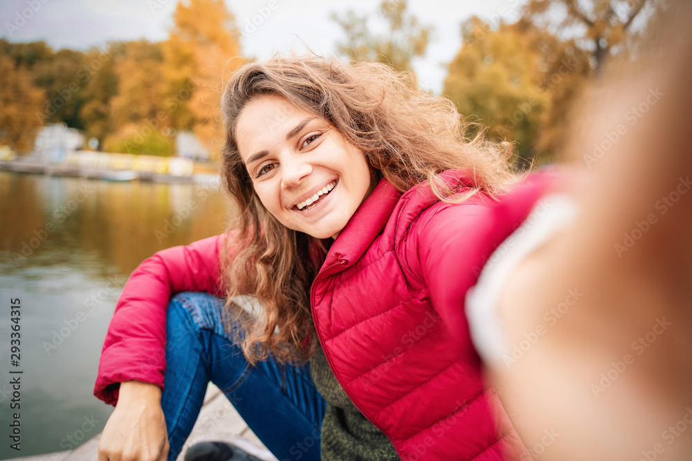 Beautiful charming young funny girl makes selfie on a smartphone in the autumn park, beauty technology fashion emotions concept Beautiful charming young funny girl makes selfie on a smartphone in the autumn park, beauty technology fashion emotions concept