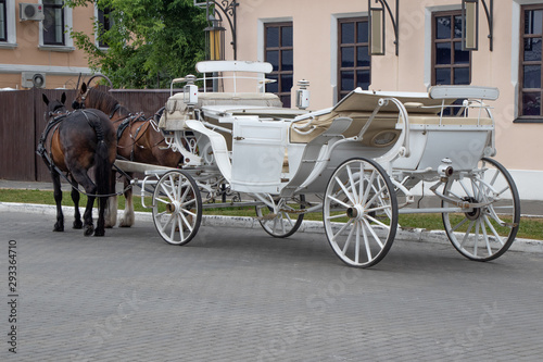 A white horse-drawn carriage with two horses, waiting for tourists on the old town square at the city of Kolomna, Russia.
