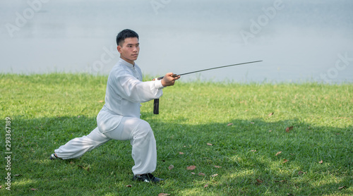 Asian man working out with Tai Chi sword in the morning at the park, Chinese martial arts, healthy care for life concept.