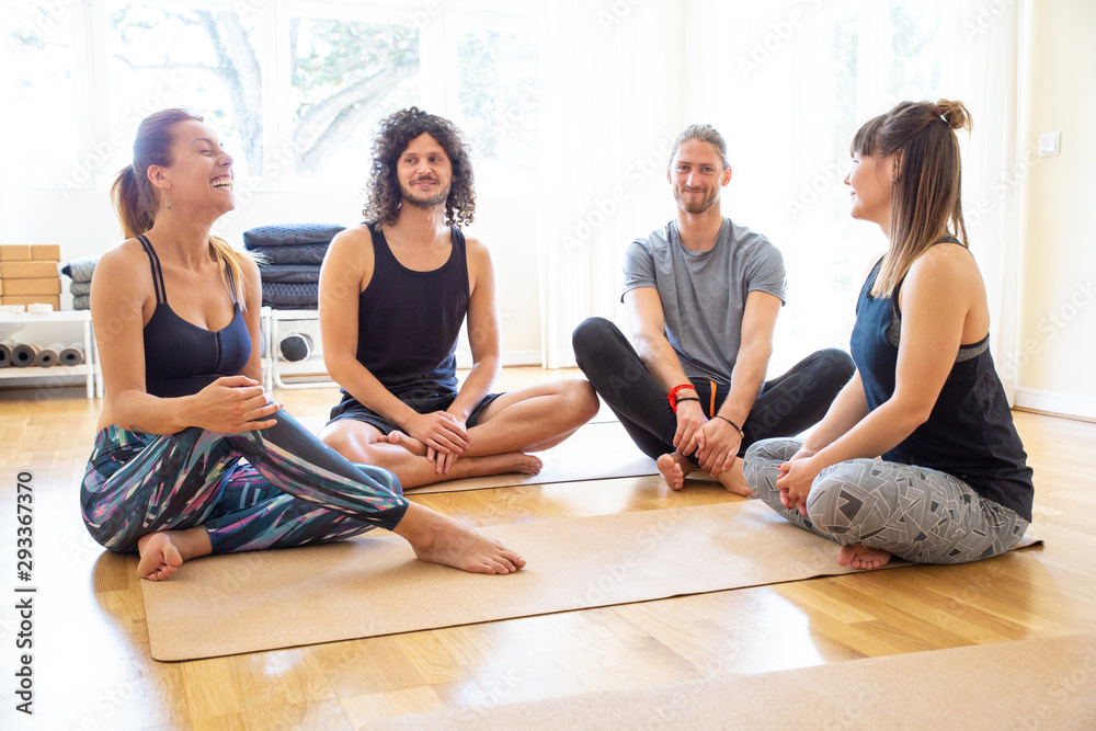 Cheerful people in yoga studio. Happy young men and women in sportswear sitting on yoga mats, talking and laughing. Yoga studio concept Cheerful people in yoga studio. Happy young men and women in sportswear sitting on yoga mats, talking and laughing. Yoga studio concept