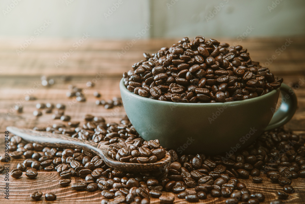 Cup full of Black coffee grains lie on a brown wooden table, background image. Coffee beans in a green cup. Cup full of Black coffee grains lie on a brown wooden table, background image. Coffee beans in a green cup.