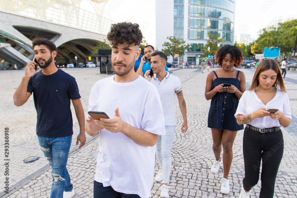 Group of people with smartphones walking down city street. Young mix raced men and woman walking outside, talking on cells, using mobile phones. Digital communication concept Group of people with smartphones walking down city street. Young mix raced men and woman walking outside, talking on cells, using mobile phones. Digital communication concept