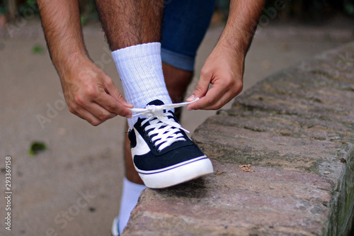 Young boy tying the shoelaces of his black and white sneakers in a park.