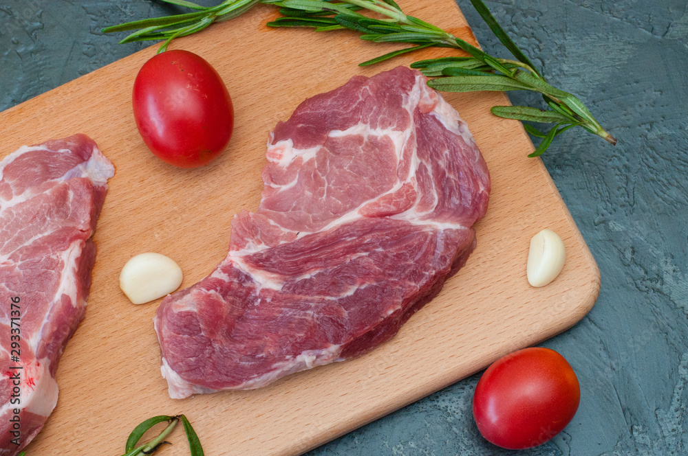 Raw meat pork steak with tomatoes garlic and rosemary on a wooden cutting board close-up, top view Raw meat pork steak with tomatoes garlic and rosemary on a wooden cutting board close-up, top view