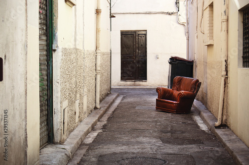 Fototapeta Naklejka Na Ścianę i Meble -  Brown leather armchair abandoned on the narrow old town street