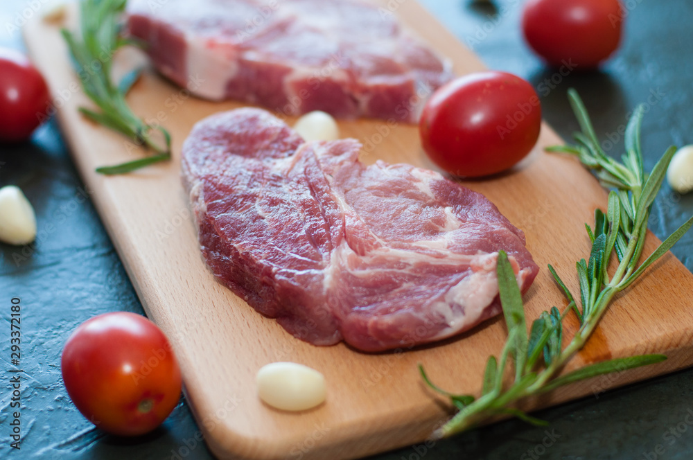 Raw juicy pork steaks with red tomatoes, rosemary and garlic on a cutting board. Raw juicy pork steaks with red tomatoes, rosemary and garlic on a cutting board.
